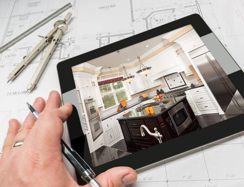 Hand of Architect on Computer Tablet Showing Custom Kitchen Photo Over House Plans, Compass and Ruler.