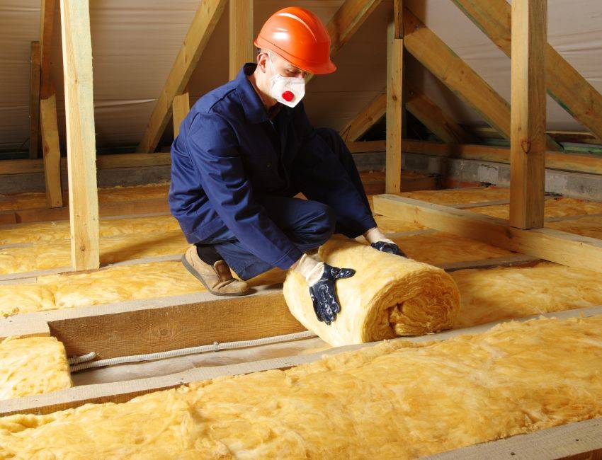 Man installing thermal roof insulation layer using mineral wool.