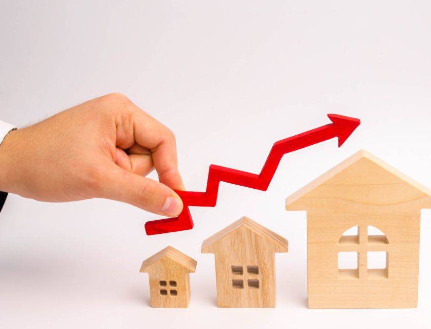 businessman's hand holds the red arrow up above the houses. The concept of growth in demand for real estate. Increase in the value of property, capital appreciation and liquidity. economic growth.