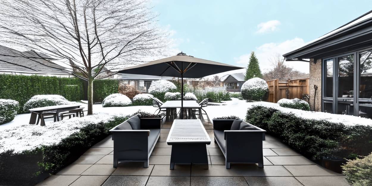 A snowy patio with a table and chairs under a canopy on a wooden floor in the backyard of a modern house.